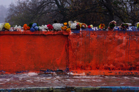 The Beta Bridge at UVA with one side painted solid orange and covered in flowers for D'Sean Perry, Lavel Davis Jr., and Devin Chandler. The wall is seen from across the street.