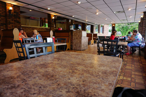 The interior of a Dairy Queen on the Greenbrier River. The walls are brown brick, the floor is geometric wood-print linoleum, the tables are a marbled taupe, and the ceiling is white acoustic tile. The image looks out over the end of one of the tables.