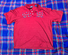 A red men's polo that says "Seek Joy" at shoulder-level with one word on either side of the button-down portion of the shirt. The text is blue, and there are embroidered blue sparkle-type stars all around each word.