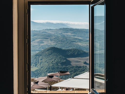 Mountain landscape viewed through a window, symbolizing the expansive visibility and access offered by a Power Portal, with rolling green hills and terrace umbrellas below under a blue sky.