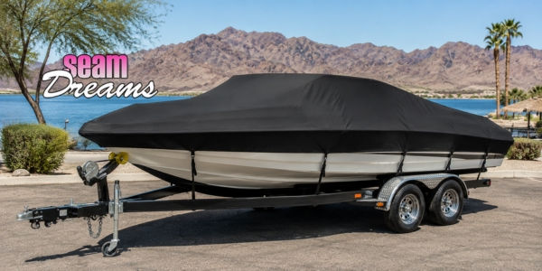Boat with black cover on trailer, parked near a lake with mountains in the background. "Seam Dreams" text in pink and white.