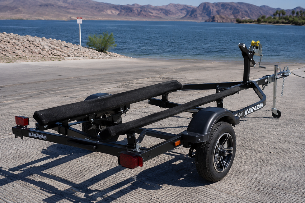 Empty boat trailer on a concrete dock by a lake, with mountains in the background. The trailer is black, branded "Karavan."