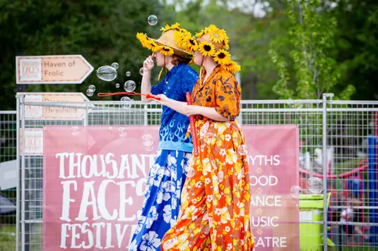 Stilt walkers in front of a Thousand Faces Festival banner