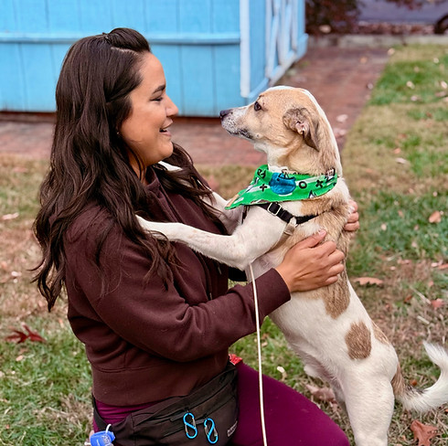 Jes kneels on the grass, scratching the back of a dog that has its front paws on her chest.