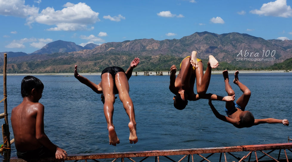 two people jumping into a body of water with mountains in the background
