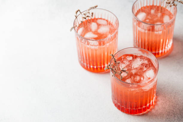 Trois verres de cocktails de rosé glacés, garnis d’herbes fines, sur une surface blanche – OTC Strawberry Spritz.