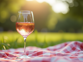 A glass of rosé on a red-and-white checkered picnic blanket in a sunny green park, with warm bokeh light.