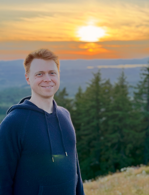 Alex Garver, somatic couples coach, standing outdoors in front of a mountain sunset