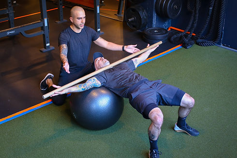 personal trainer coaching a male client how to perform a supine lateral ball roll exercise in a gym