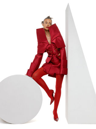 Full-length editorial view of the Obsidian Bloom conceptual red look posed among geometric white forms, featuring its dramatic collar, corseted waist and layered silhouette by Samanta X Designer