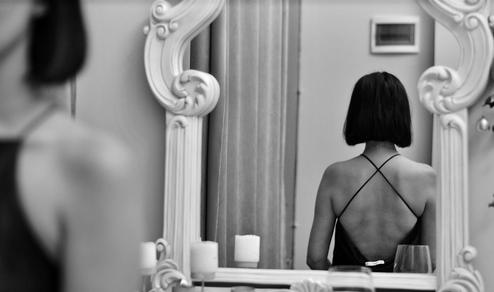 Woman standing in front of a mirror with an open-back dress, symbolizing reflection and personal transformation in a one-on-one life coaching journey with a nurse and life coach.