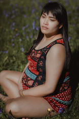 A pregnant woman sitting cross legged on the grass, among bluebells on a maternity photoshoot in Sussex