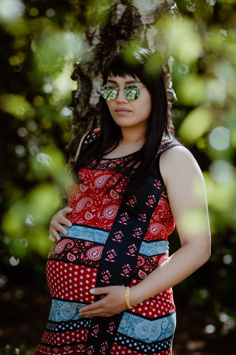 A young woman cradling her baby bump standing beside a tree on a maternity photoshoot in West Sussex