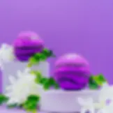 Two Purple and Dark Purple Blackberry Fruity Bath Bomb on white plinths with white flowers and a purple background