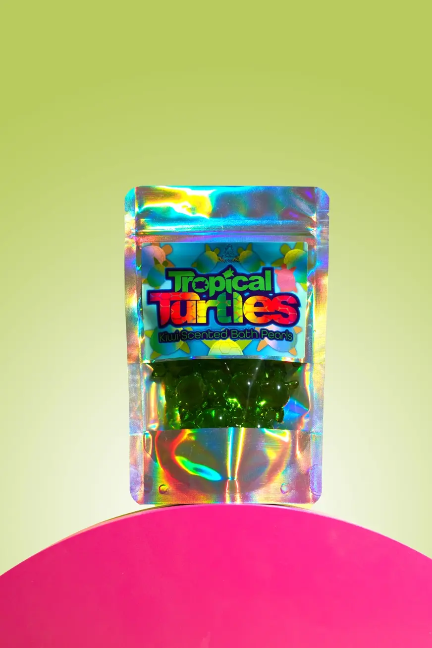 Resealable plastic packet containing green turtle bath pearls with yellow background on a red stand
