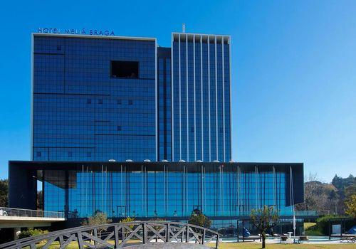 Wide landscape photo of the exterior of the modern glass-fronted Meliá Braga hotel under a clear blue sky.