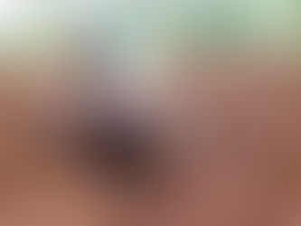 An older woman with visible wrinkles squats in the soil, her sari pulled over her head as she works in the field.