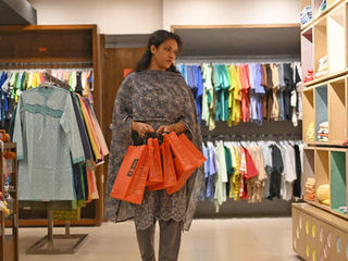 A woman holds five Aarong paper shopping bags in her hands, walking in a clothing store.