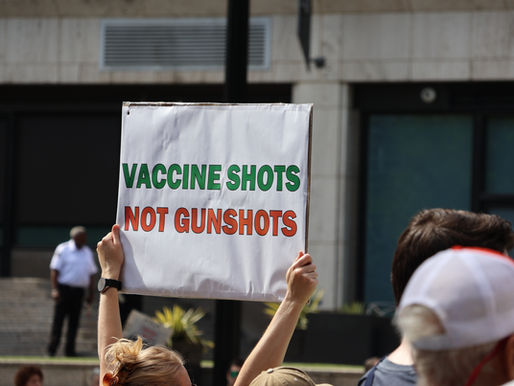 A protester holds up a “VACCINE SHOTS NOT GUNSHOTS” sign