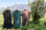 Three women hold up the abayas they made in a grassy patch