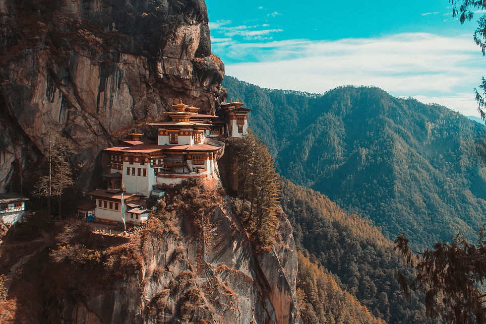 A monastery sits on a cliff in Bhutan, with lush green forests below.