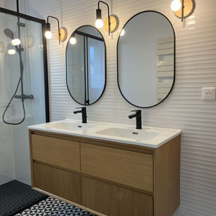 Salle de bain avec un meubles doubles vasques suspendu n bois et blanc, deux miroirs ovales au dessus et des luminaires posés en applique sur le mur.