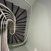 Vue en plongée d'un escalier hélicoïdal blanc, avec une main courante en acier, fixée au mur et au garde-corps.
