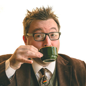 A man in glasses wearing an academic suit sips tea.