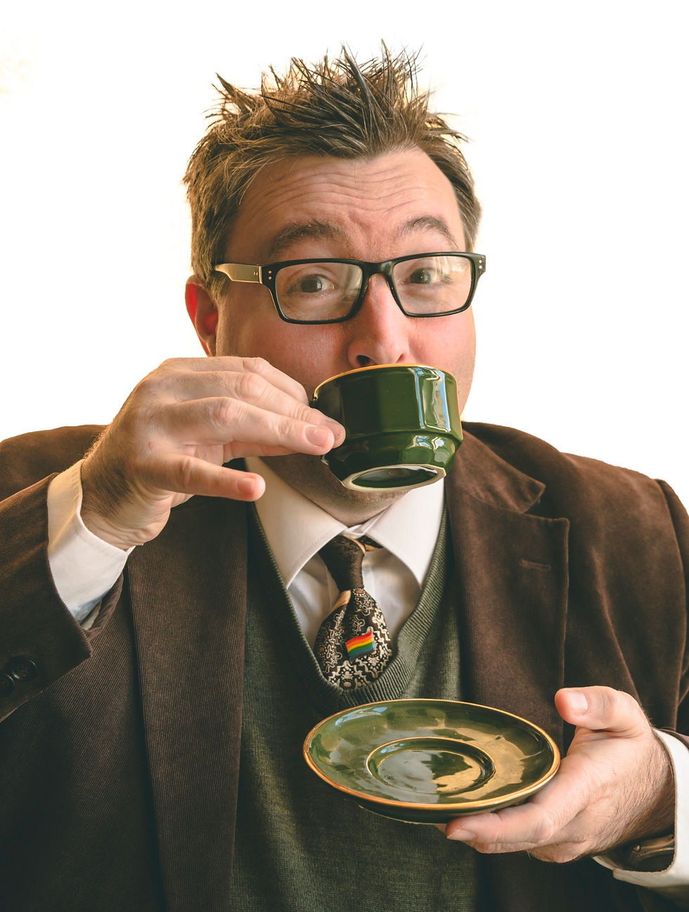 A man in glasses wearing an academic suit sips tea.