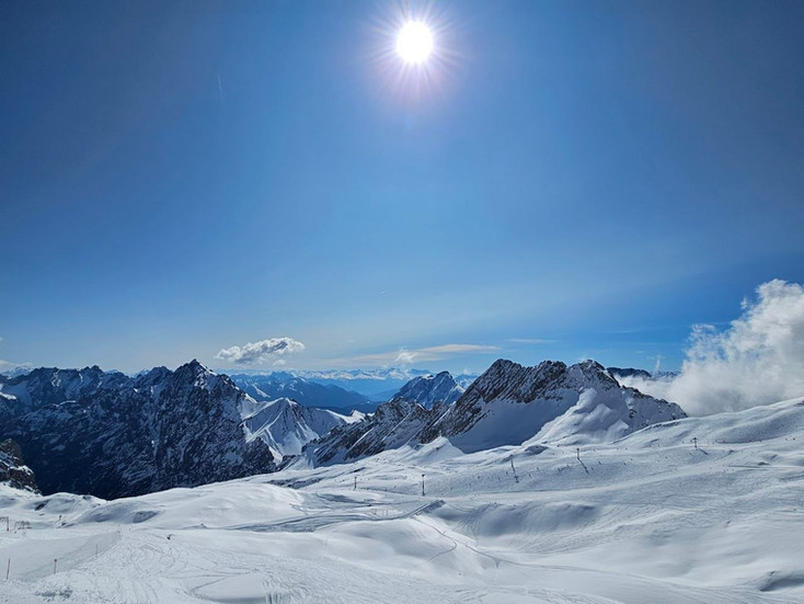Sunny winter view from Zugspitze with snowfields and mountains in the distance.