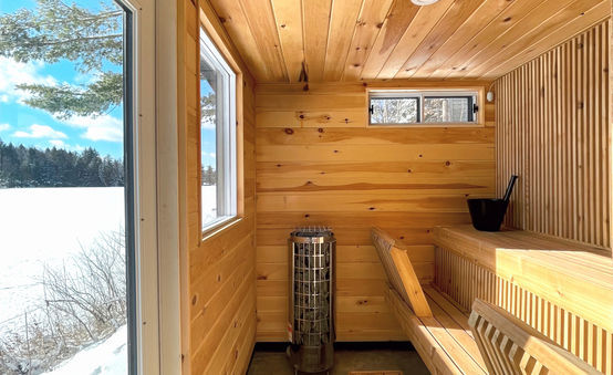 A wooden sauna interior with a large window viewing a snowy landscape and a metal heater