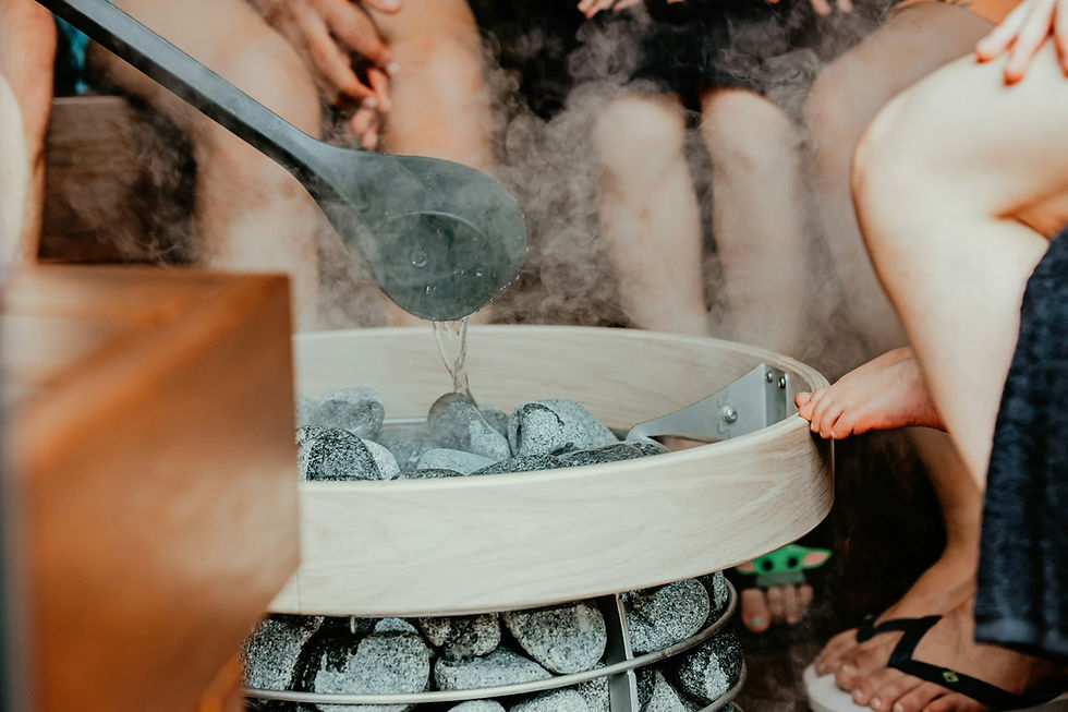 A ladle pouring water over hot sauna stones, creating steam, with people sitting nearby