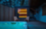 An outdoor hot tub glowing blue next to a modern backyard sauna cabin at night