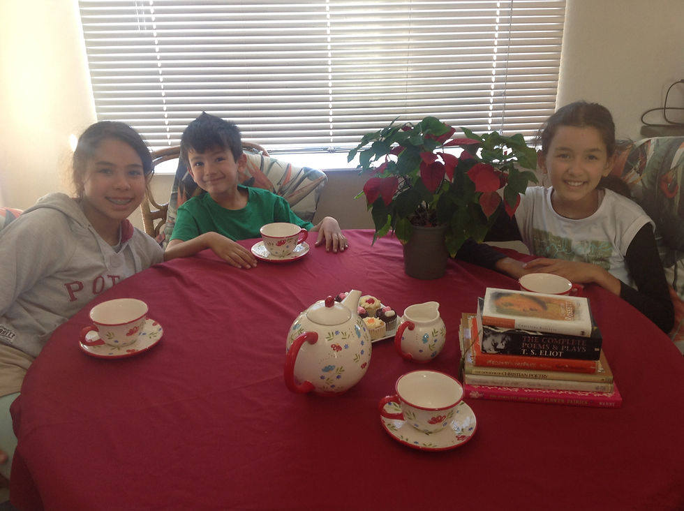 children sitting at table with red tablecloth, tea set and pot plant