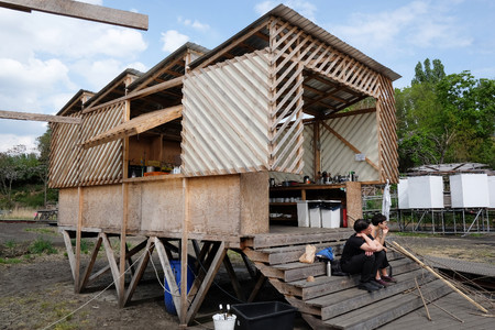 A wooden structure on stilts at the Floating University. Two people are sitting on the steps.