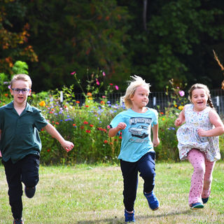Three children running and playing on a grassy field.