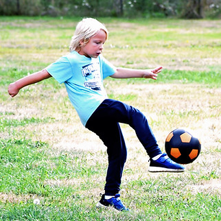 A boy kicking a soccer ball on a grassy field.