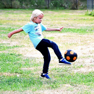 A boy kicking a soccer ball on a grassy field.