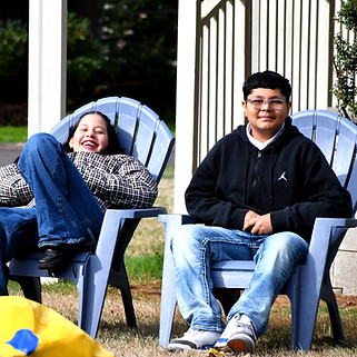 Two smiling students relaxing in blue Adirondack chairs.