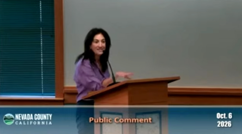 white woman with brown hair and purple shirt speaks at a podium at a board of supervisor meeting