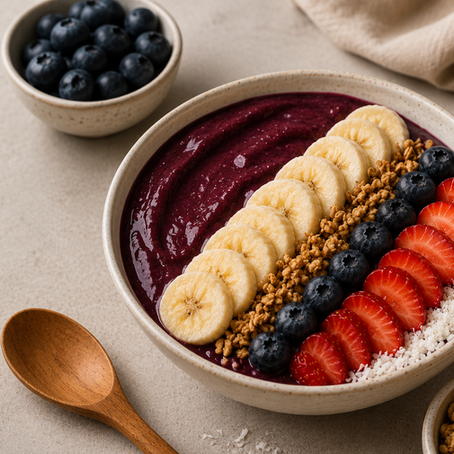 Bowl de açaí servido com banana, morango, mirtilos, granola e coco ralado sobre superfície clara, em composição minimalista e sofisticada com luz natural