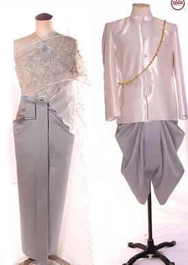Traditional Thai wedding couple set in silver grey tones featuring a Thai silk bride skirt with sheer bead-embroidered sabai and silver belt, paired with a light silver silk groom jacket and grey chong kraben with gold chain accessory, displayed on mannequins against a white background.