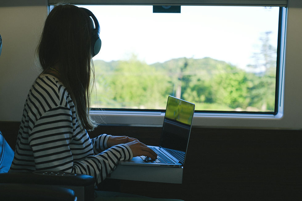 Woman gazing out the train window with her hands resting on her laptop keyboard.