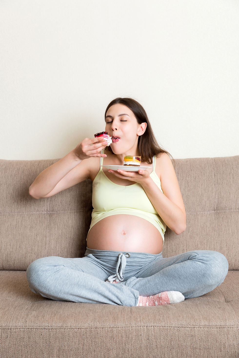 hungry pregnant woman is eating tasty desserts sitting sofa home