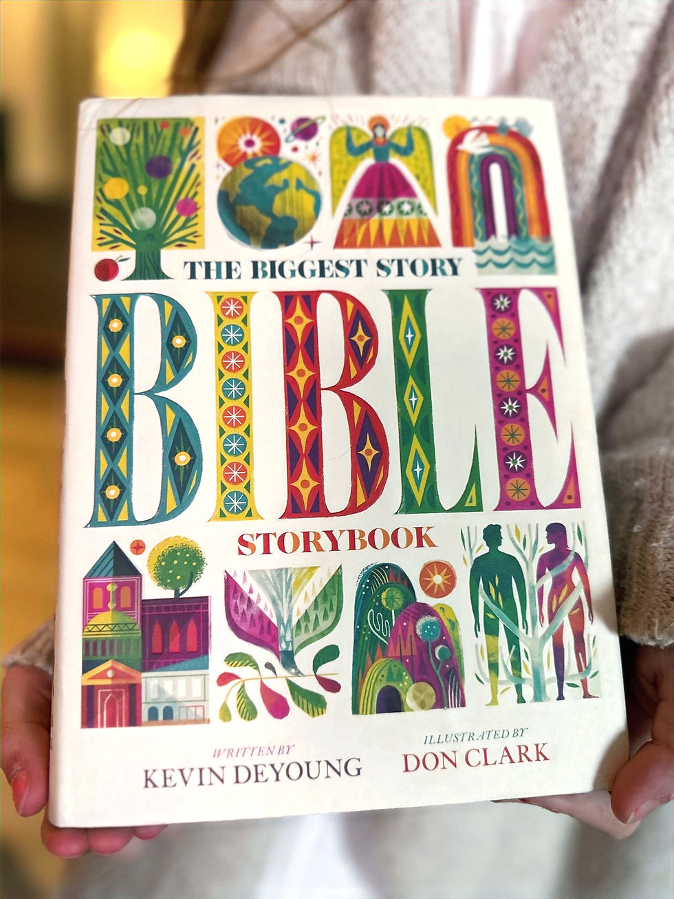 Person holding "The Biggest Story Bible Storybook" with colorful illustrations. Text includes author Kevin DeYoung and illustrator Don Clark.