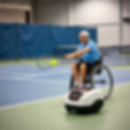 a person on wheelchair playing tennis in a court with a ball serving machine in front of h