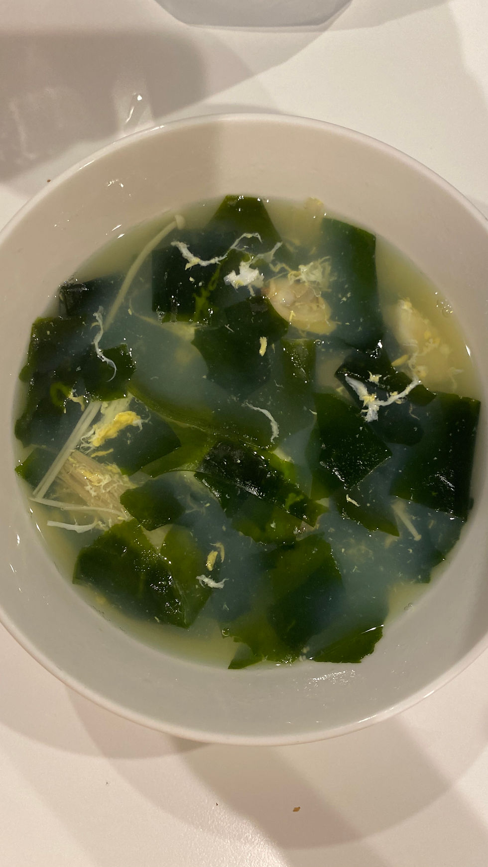 Vibrant bowl of green seafood wakame soup with fresh leafy greens in a white bowl—healthy low-carb diet recipe.
