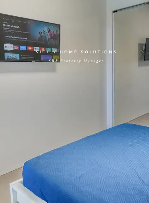 Camera moderna con due letti blu, TV a parete HOME SOLUTIONS Property Manager.