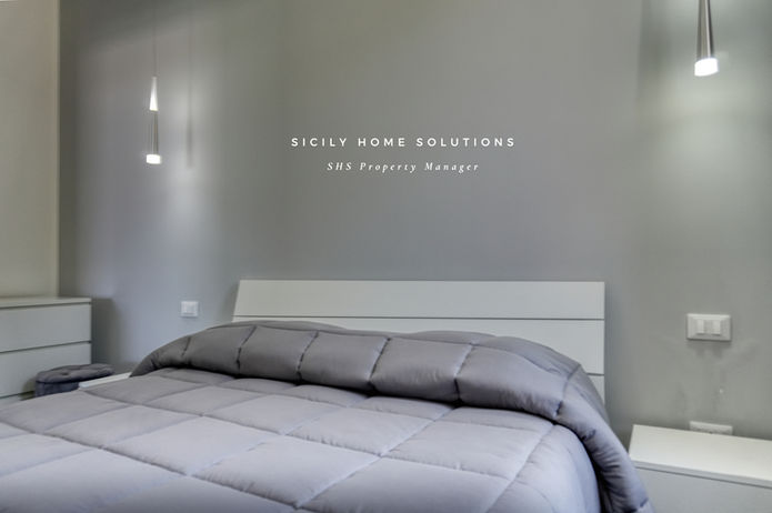 Camera da letto con parete grigia e testo Sicily Home Solutions. ville deluxe
