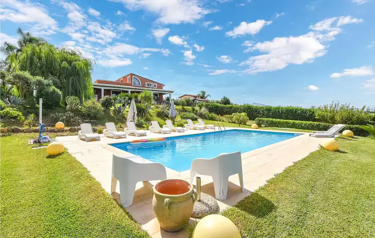 Affitto villa con piscina, vista mare, giardino verde e cielo azzurro.